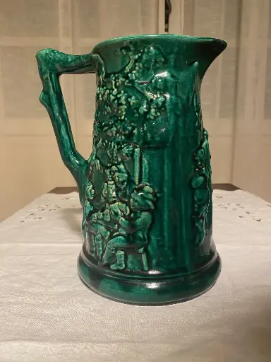 Cruche en barbotine signée Sarreguemines, superbe carafe verte et intérieur bleu, au décors de personnages, XIXème siècle. Juste un petit choc au bec.                           Barbotine jug signed Sarreguemines, superb green carafe and blue interior, with character decorations, 19th century. Just a small shock to the spout.
