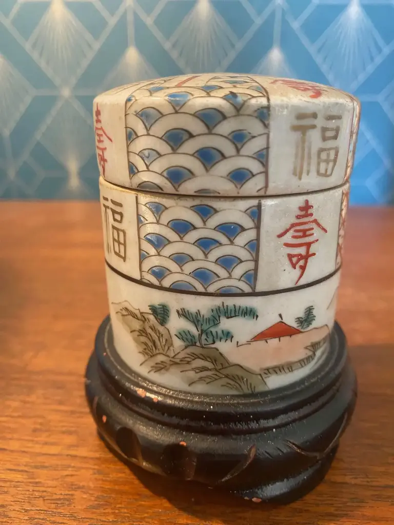 Très jolie boîte de Chine, en porcelaine et forme tube à décor de montagnes, de paysages et de formes géométriques. Boîte à couvert sur son socle en bois noirci elle est  en bon état peinte à la main bien sur. Elle mesure 10cm de haut pour 6 de diamètre socle compris, qui ne s'enlève pas.                                          Very pretty Chinese box, in porcelain and tube shape decorated with mountains, landscapes and geometric shapes. Cutlery box on its blackened wooden base, it is in good condition, hand-painted of course. It measures 10cm high by 6 in diameter including the base, which cannot be removed.